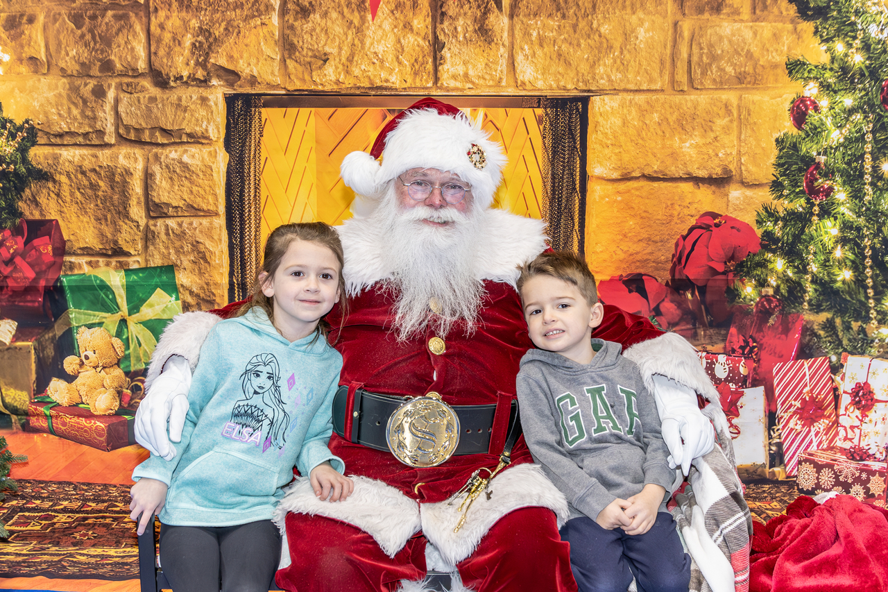 Santa sits with a boy and a girl in front of a fire place at Marple Sports Arena
